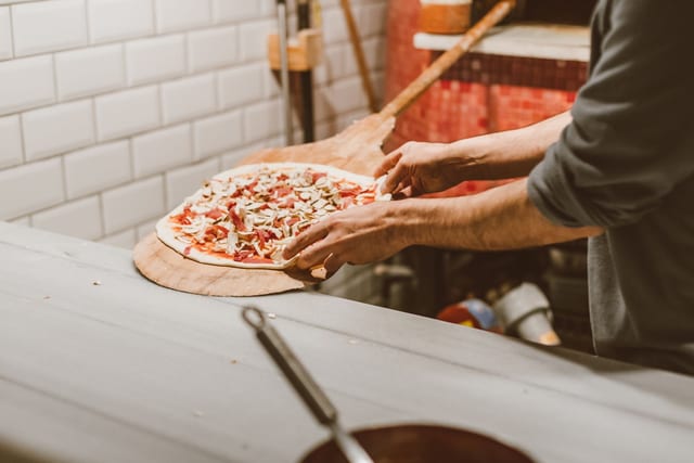 Ruke slažu pizzu na drvenu lopatu ispred peći (ilustrativna fotografija)